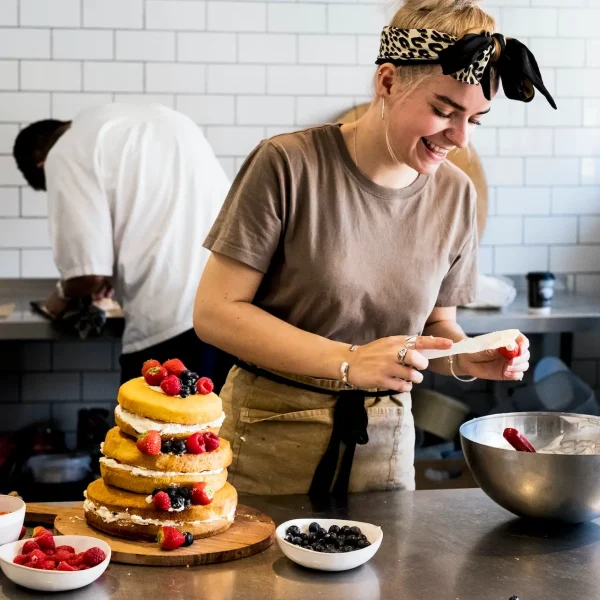 a-cook-working-in-a-commercial-kitchen-assembling-a-layered-sponge-cake-with-fresh-fruit-.jpg